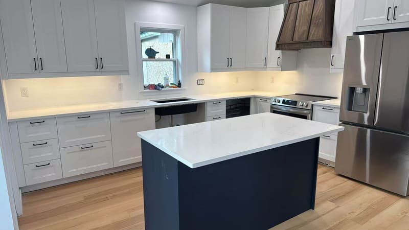 Navy blue island topped with white quartz beside pale cabinets